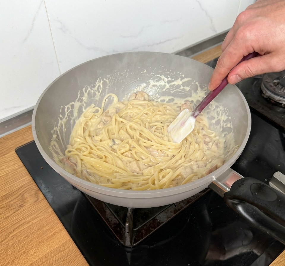 Mieszanie makaronu linguine w gęstym sosie z kawałkami boczku i pieczarek.