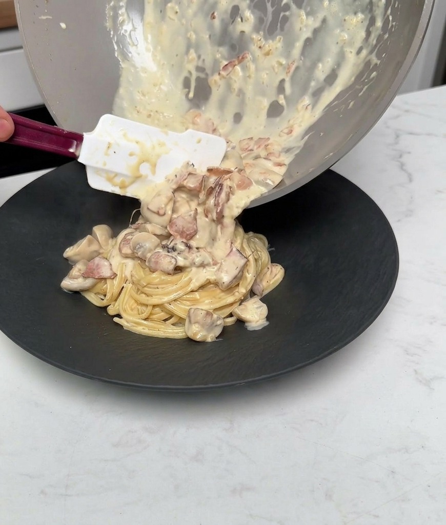 Polewanie makaronu resztą sosu śmietanowego z boczkiem i pieczarkami z patelni.