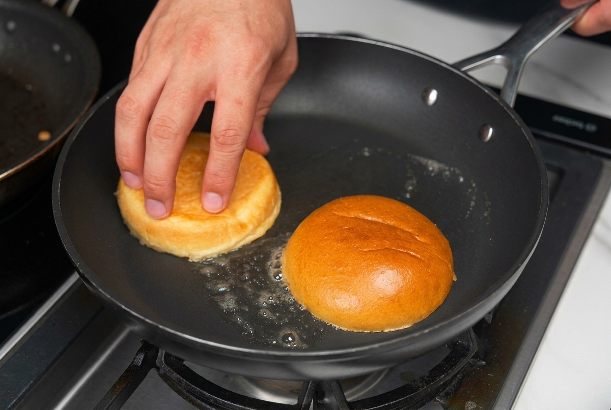 Połówki bułek do burgerów ułożone wnętrzem do dołu na patelni ze skwierczącym, roztopionym masłem.