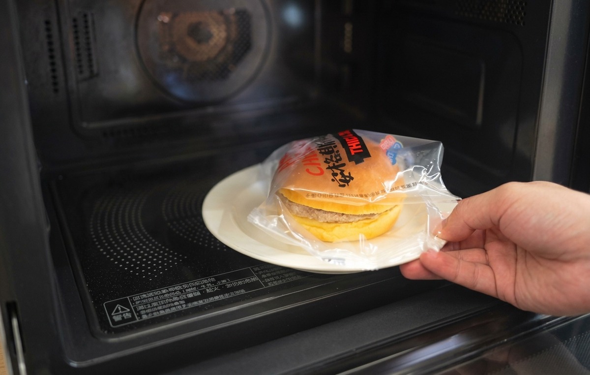 Dłoń nakładająca górną połówkę podpieczonej bułki brioche na burgera z cebulą i roztopionym serem.