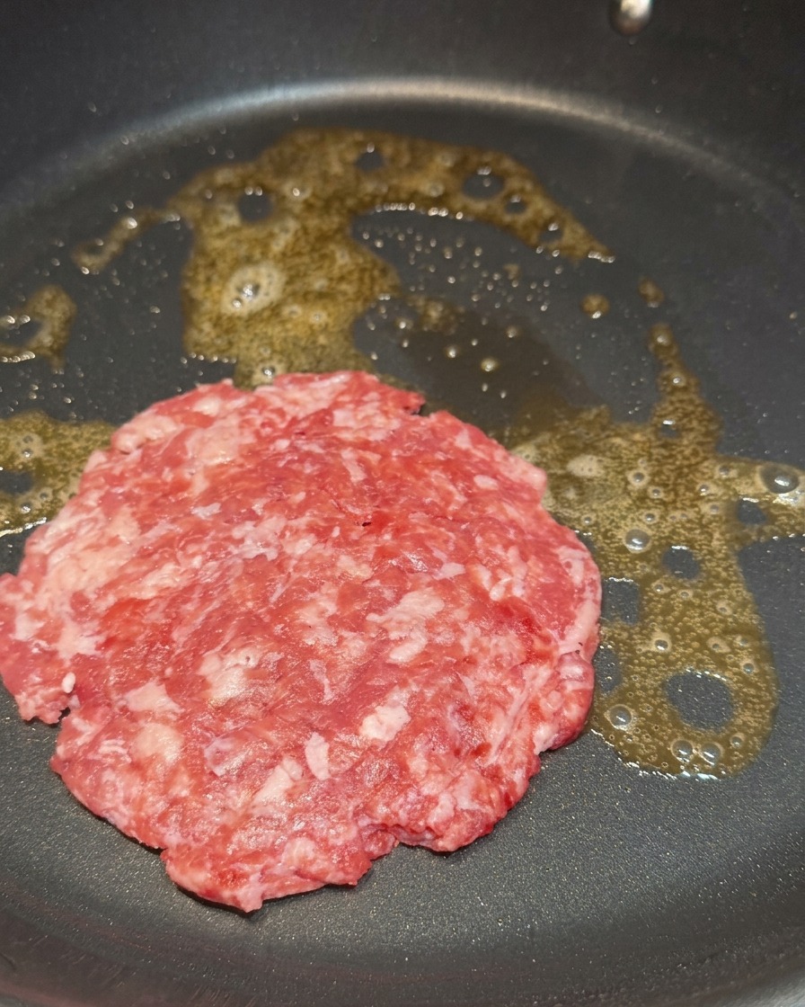 Surowy, marmurkowy kotlet wołowy smażący się na roztopionym maśle na czarnej patelni.