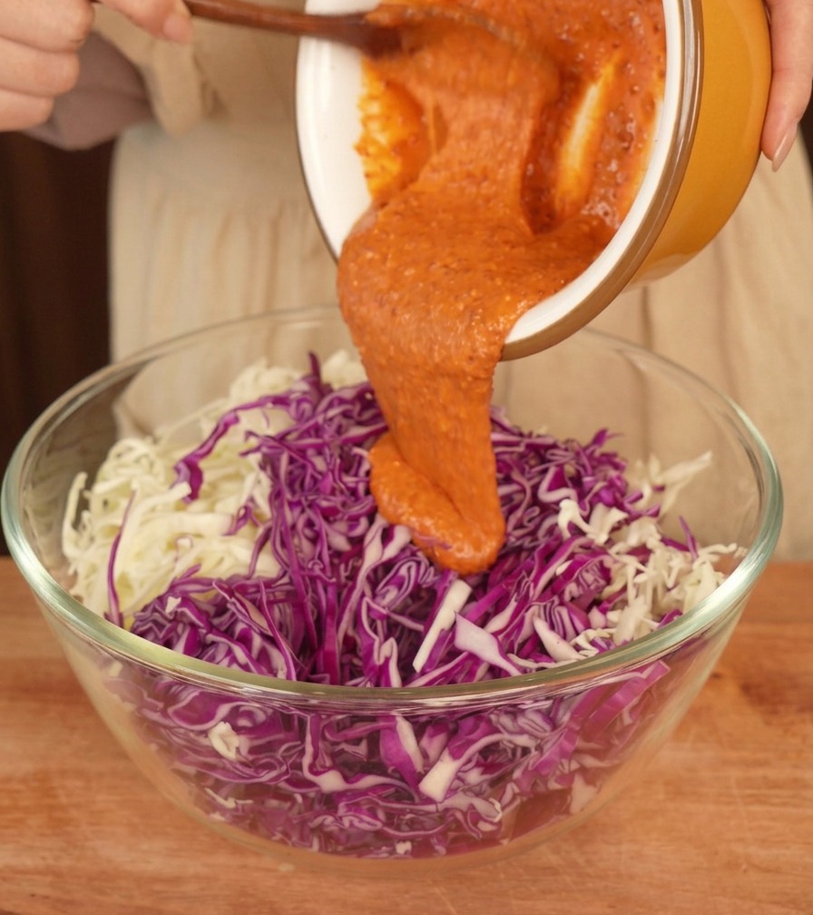 Pomarańczowy dressing wylewany na poszatkowaną białą i fioletową kapustę w szklanej misce.
