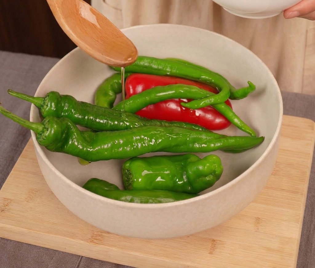 Czysty olej roślinny lany z drewnianej łyżki na mieszankę świeżych czerwonych i zielonych papryczek chili w jasnej misce.