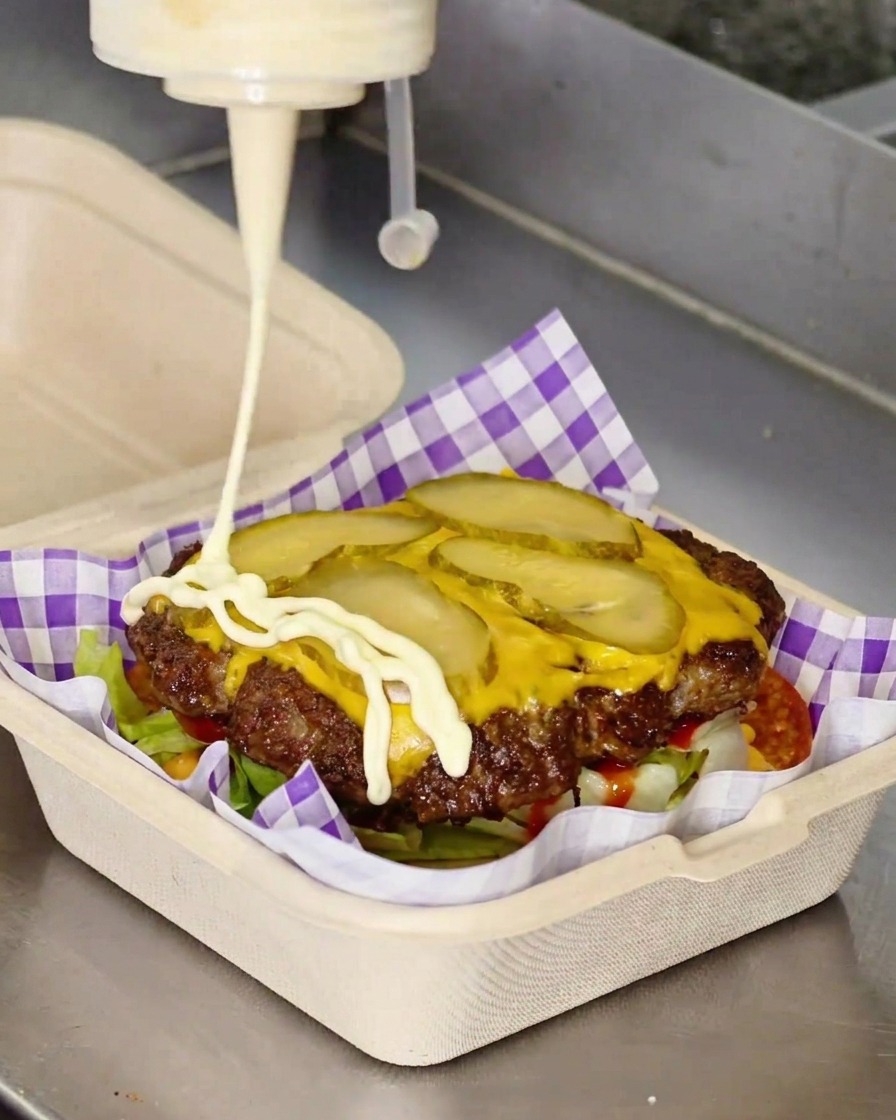 Biały majonez wyciskany z butelki w zygzakowaty wzór na kotlet z serem.