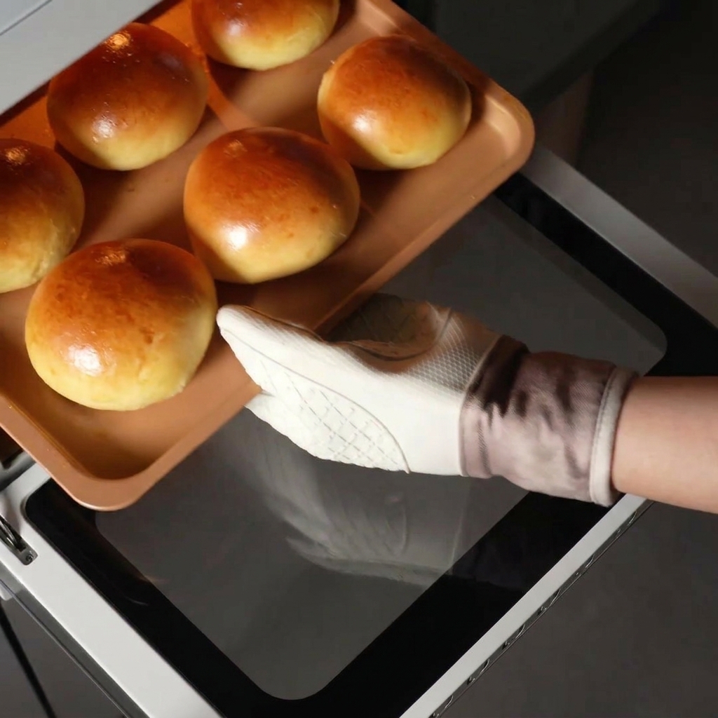 Dłoń wyciągająca blachę z idealnie upieczonymi bułkami brioche z gorącego piekarnika.
