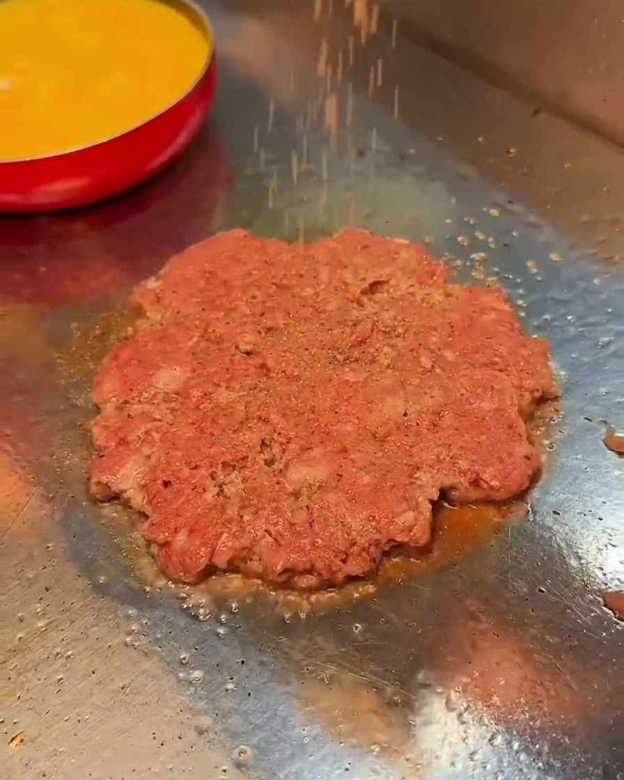 Sól i czarny pieprz sypane na smażący się kotlet wołowy na gorącej płycie.