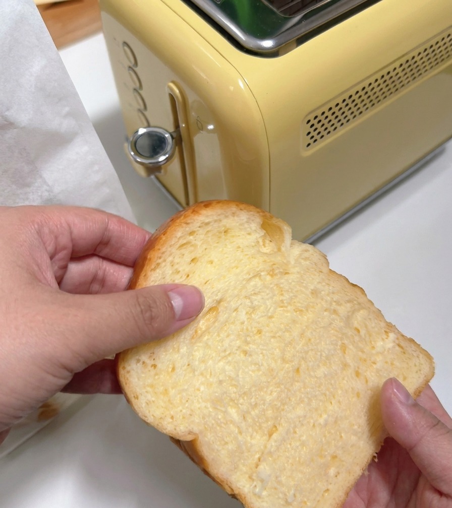 Osoba wkładająca grubą kromkę białego chleba do żółtego tostera w stylu retro.