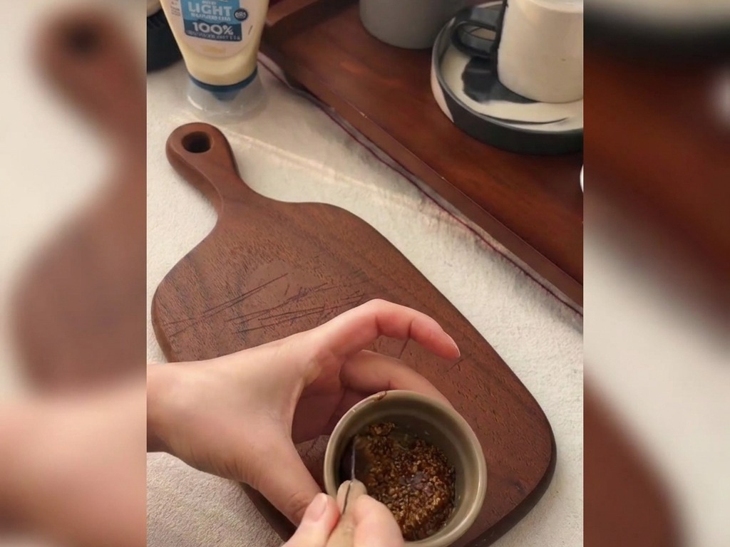 Ręce mieszające łyżeczką musztardę ziarnistą z miodem w małej miseczce na drewnianej desce.