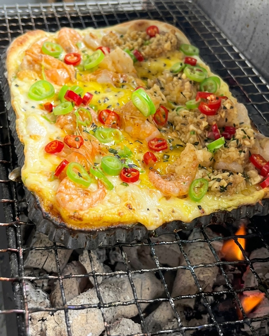 Prostokątny spód pizzy z krewetkami i warzywami piekący się nad żarzącymi się węglami drzewnymi.