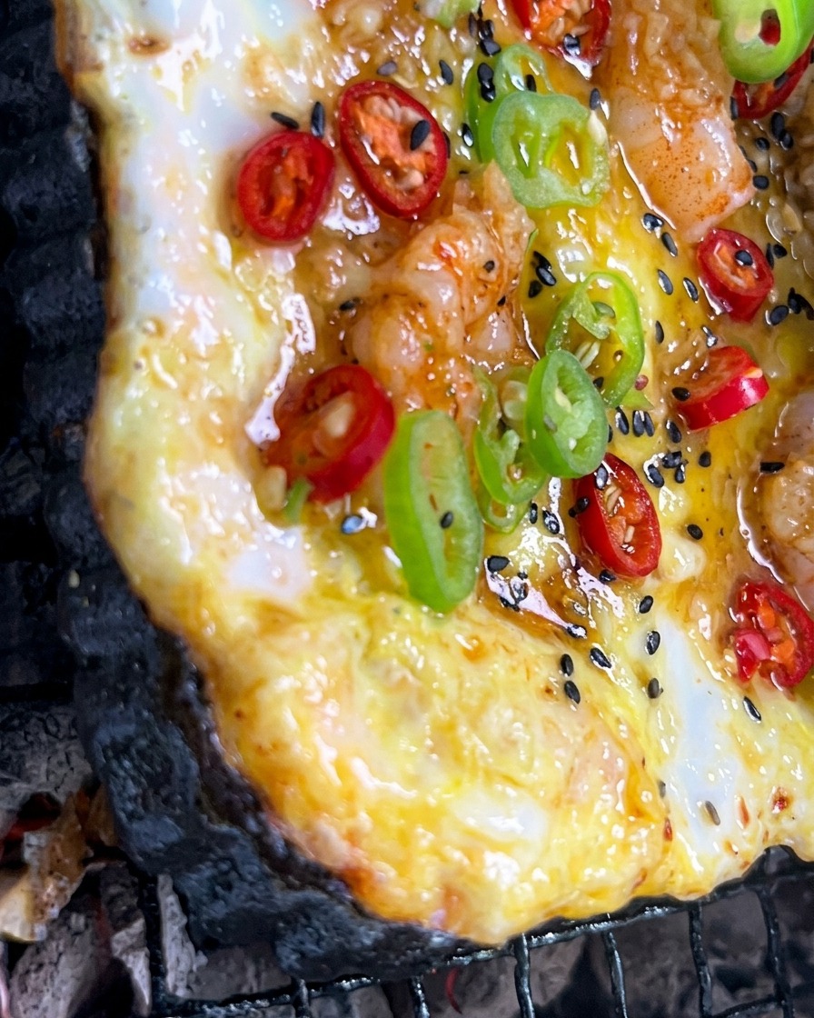 Sos z posiekanego czosnku nakładany pędzelkiem na kolorową pizzę piekącą się na grillu węglowym.