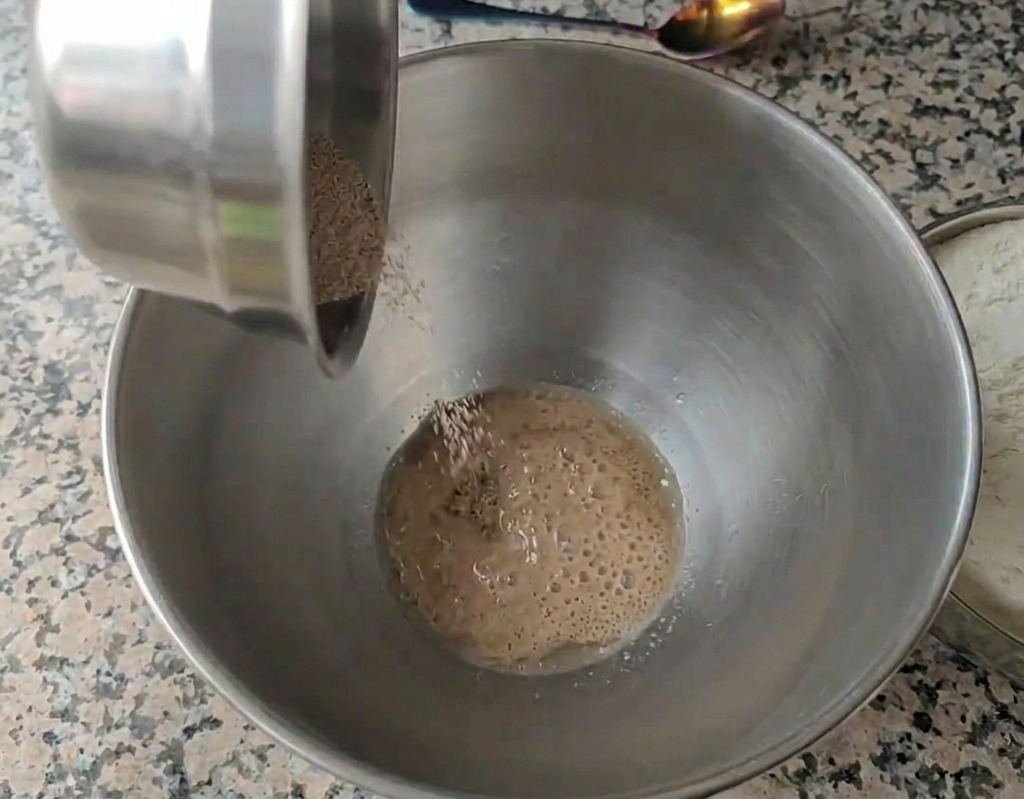 Suche drożdże granulowane wsypywane do misy ze stali nierdzewnej napełnionej wodą, z widocznymi małymi bąbelkami na powierzchni.