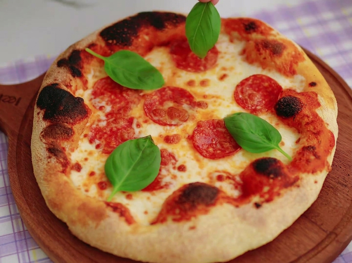 Dłoń układająca świeże, zielone liście bazylii na upieczonej pizzy neapolitańskiej z rumianym brzegiem i stopionym serem.