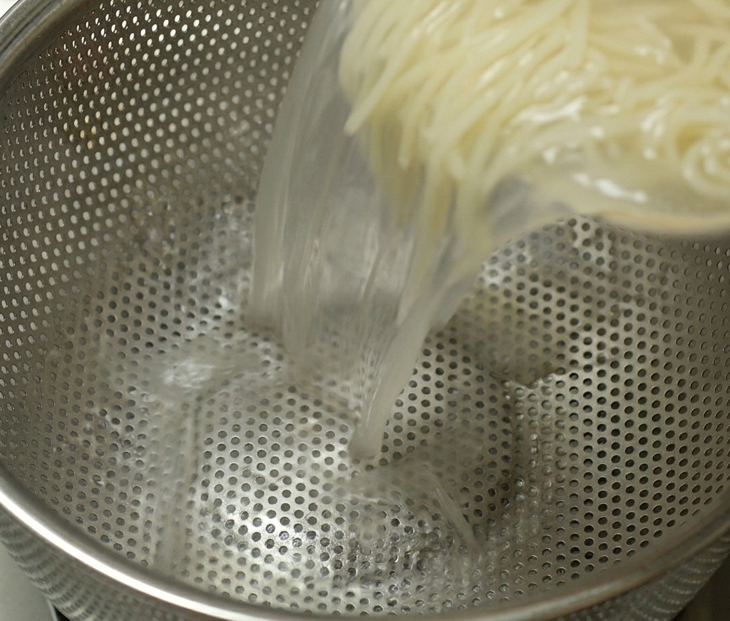 Ugotowany makaron ramen wlewany z garnka do durszlaka ze stali nierdzewnej w celu odcedzenia wody.