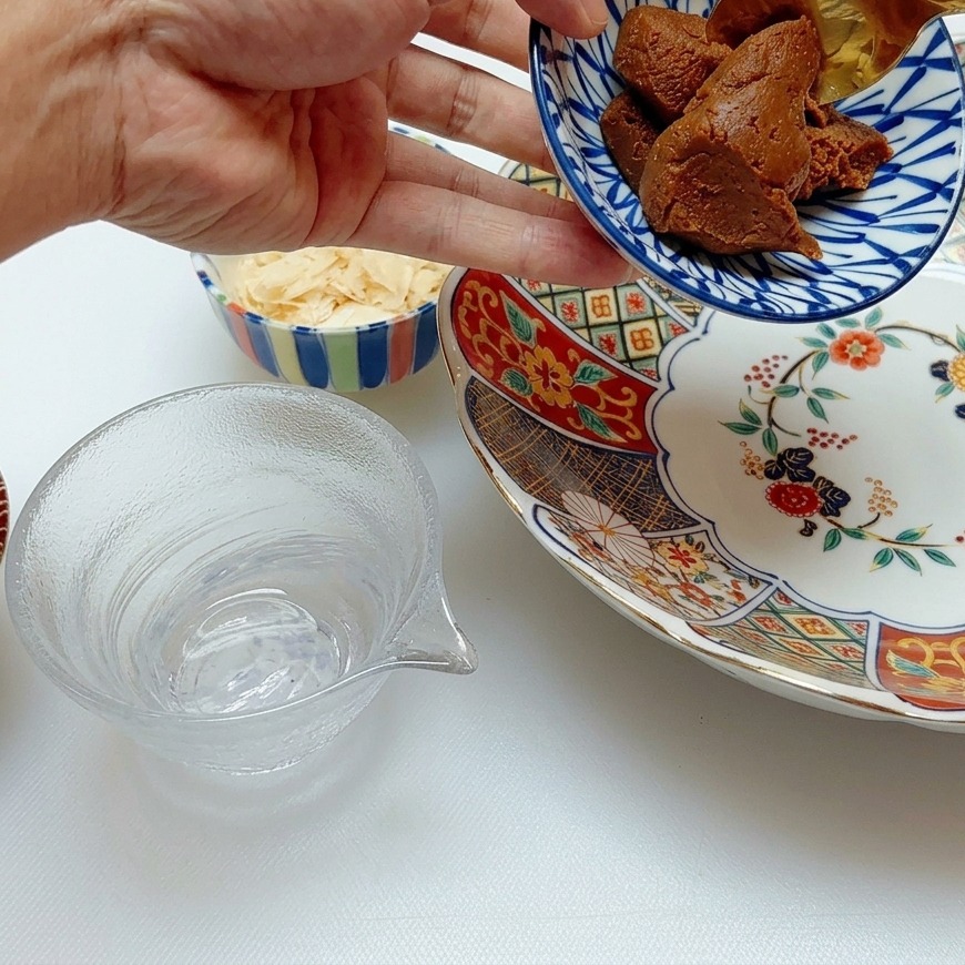 Złota łyżka nabierająca gęstą, esencjonalną ciemną pastę miso do porcelanowej miski w niebiesko-białe wzory.