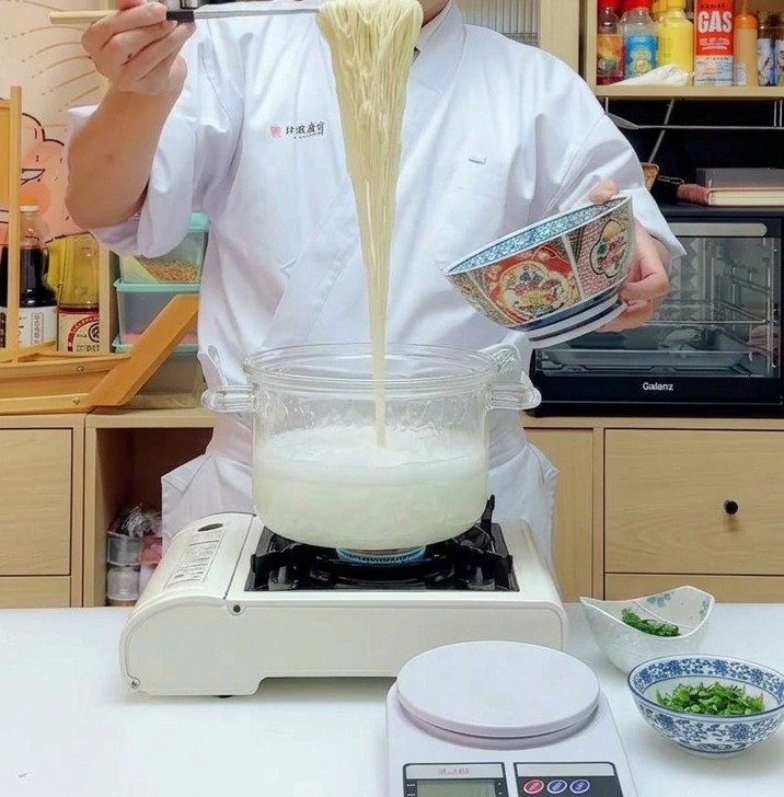 Porcja długiego, żółtego makaronu ramen wyciągana wysoko pałeczkami z parującego garnka.