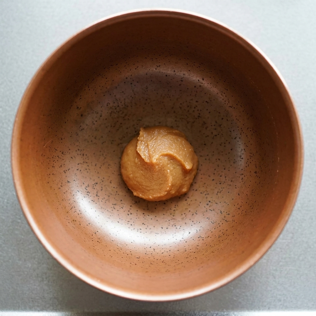 Porcja gęstej, brązowej pasty miso na dnie nakrapianej ceramicznej miski.