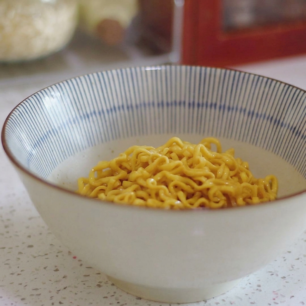 Gotowy ramen w ceramicznej misce w niebiesko-białe paski, udekorowany dodatkami.