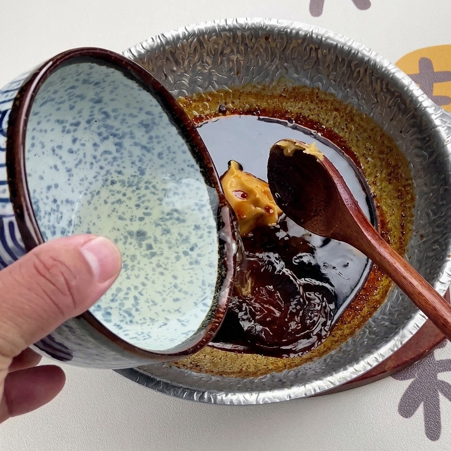 Klarowny bulion dashi wlewany z biało-niebieskiej ceramicznej miski we wzory do ciemnego sosu miso.