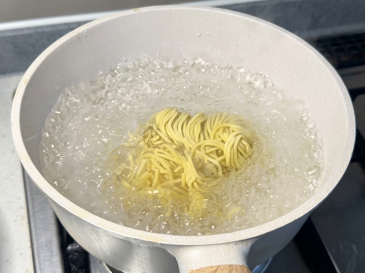 Świeży, żółty makaron ramen mocno gotujący się we wrzątku w jasnym garnku.