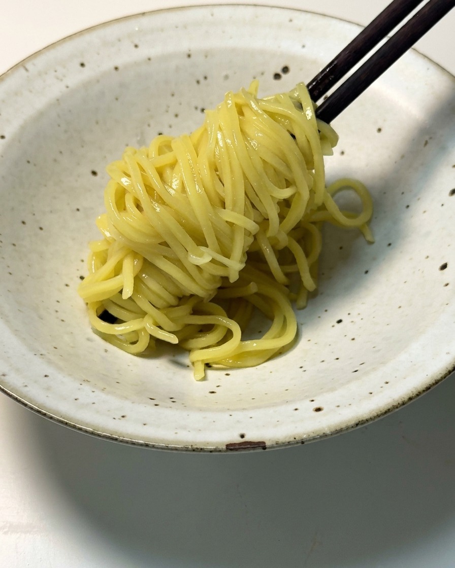 Ugotowany makaron ramen nakładany przy pomocy ciemnych drewnianych pałeczek do płytkiej miski.