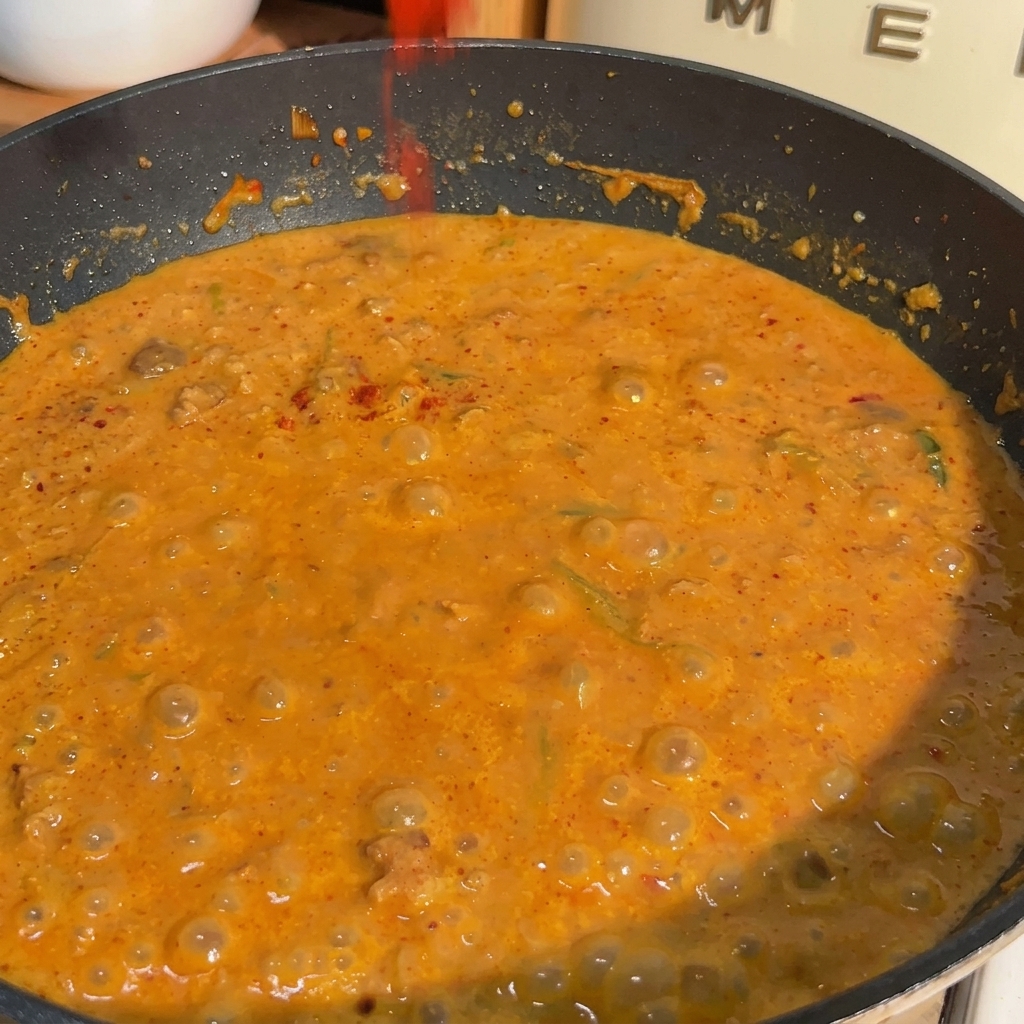 Patelnia wypełniona bulgoczącym pomarańczowym sosem z miso i mleka sojowego, posypywana czerwonym chili w proszku.