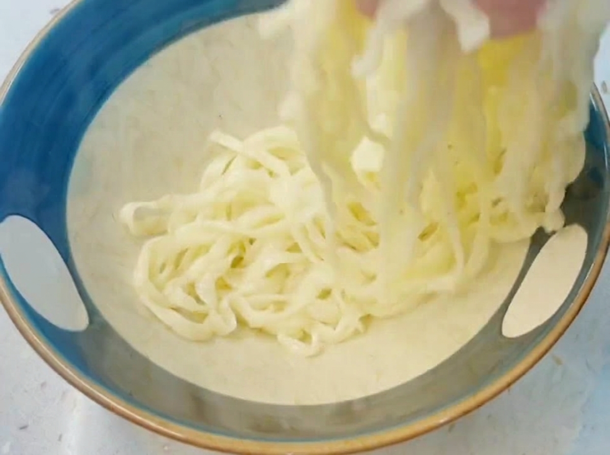 Dłoń podnosząca i hartująca gruby, ugotowany biały makaron ramen w niebieskiej misce wypełnionej zimną wodą.