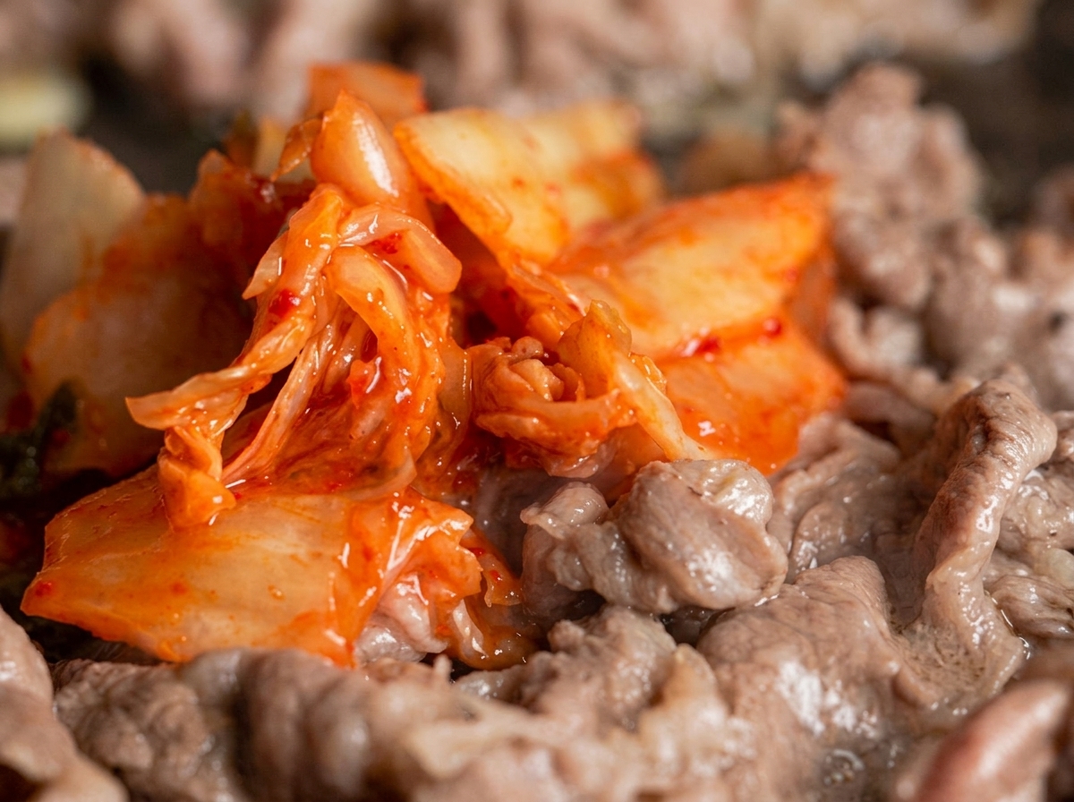 Porcja intensywnie czerwonego kimchi mieszana z cienkimi paskami wołowiny na patelni.