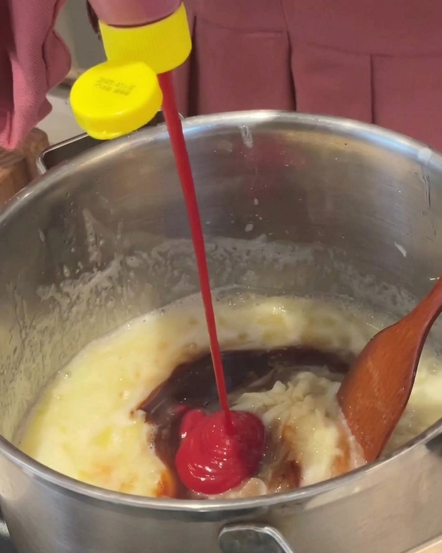 Gęsty, czerwony ketchup wyciskany z butelki do bulgoczącego brązowego sosu w metalowym garnku.