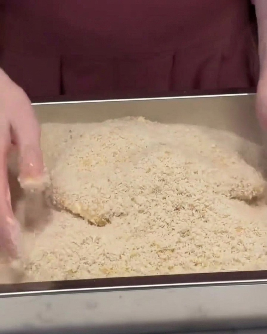 Kotlet schabowy zasypywany i dociskany w metalowej blaszce pełnej chrupkiej panierki panko.