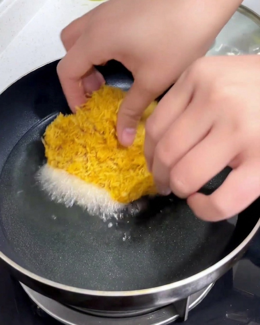 Kotlet schabowy w panierce wkładany ostrożnie dłonią na patelnię z gorącym, mieniącym się olejem.