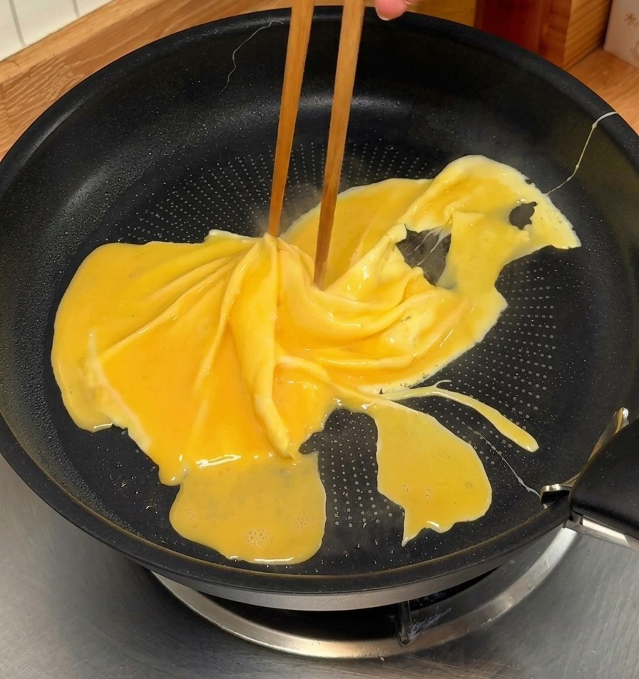 Pałeczki obracające częściowo ścięty żółty omlet na czarnej patelni nieprzywierającej w celu stworzenia spiralnego wzoru.