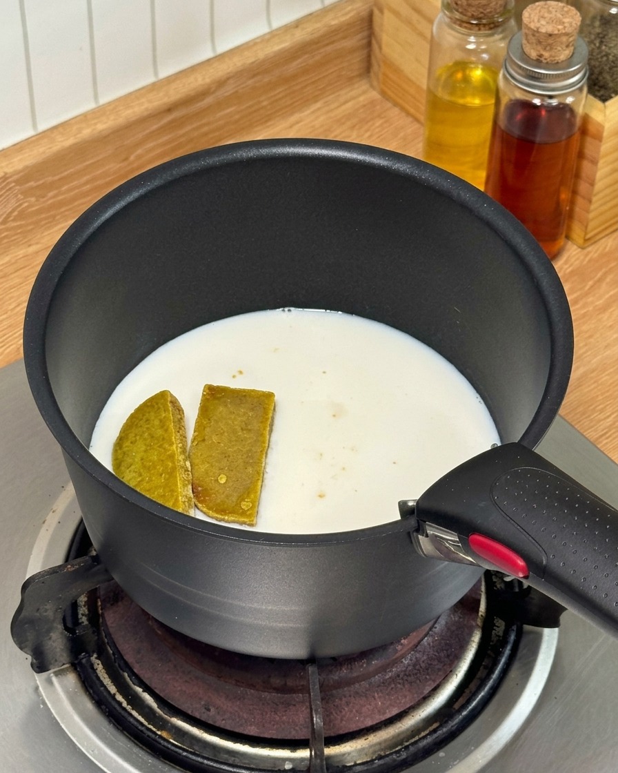 Kostki curry i mleko podgrzewane w małym czarnym rondelku na kuchence gazowej.