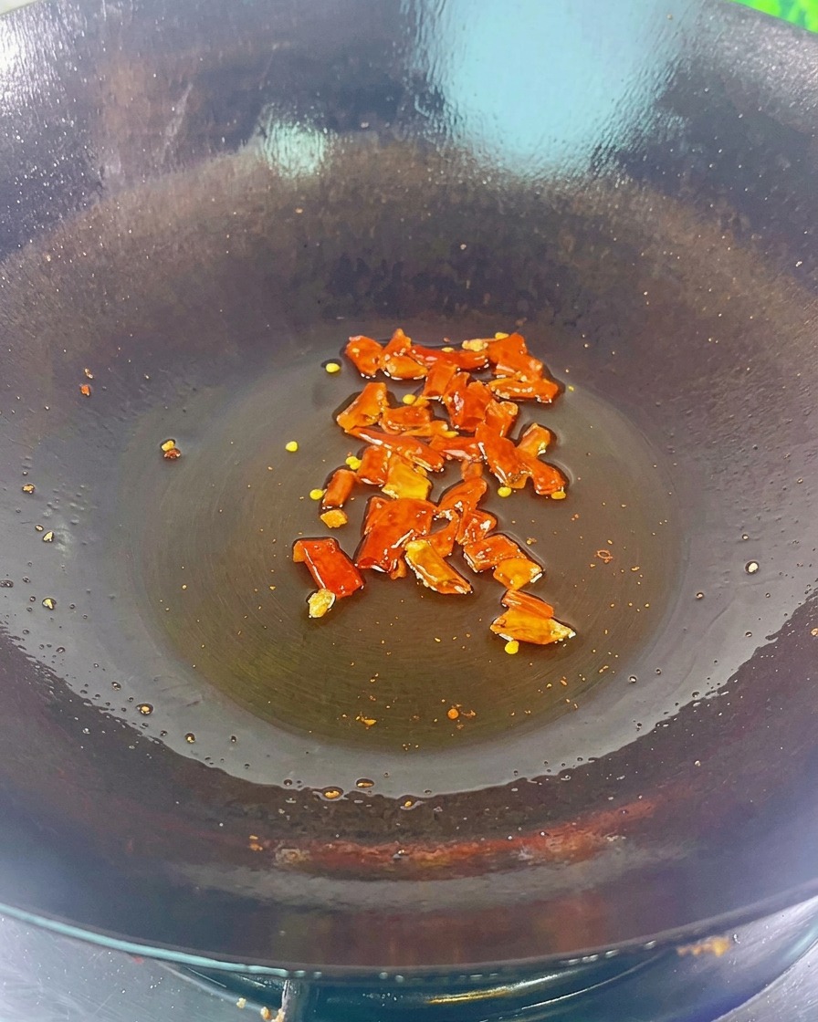 Kawałki suszonego chili i czarna fasola skwierczące na dnie ciemnego woku z cienką warstwą oleju.