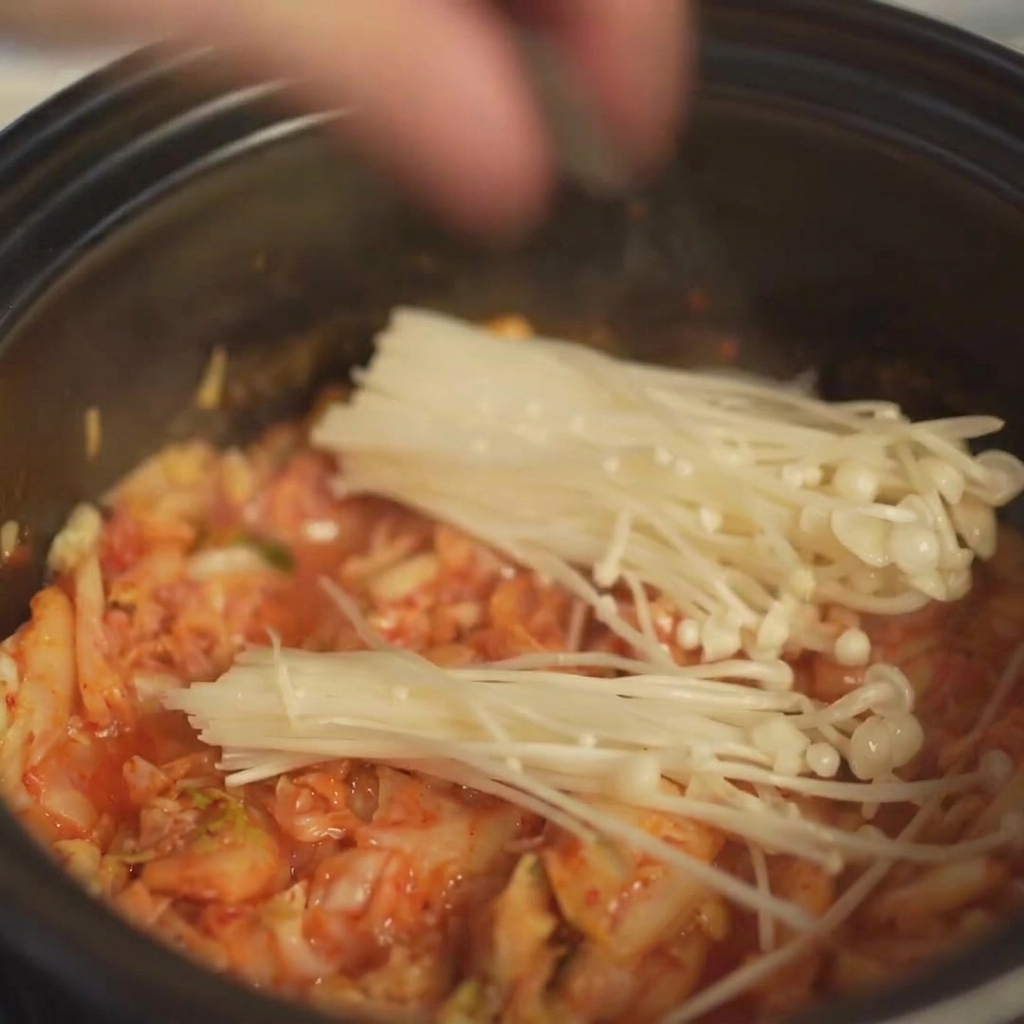 Układanie pęczka świeżych grzybów enoki w garnku bezpośrednio na warstwie kimchi.