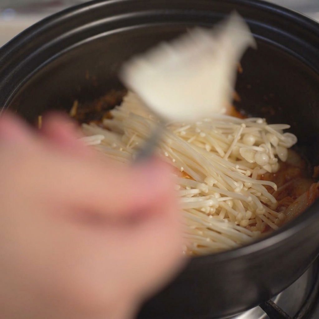 Nakładanie łyżką dużych kawałków miękkiego, białego tofu do garnka.