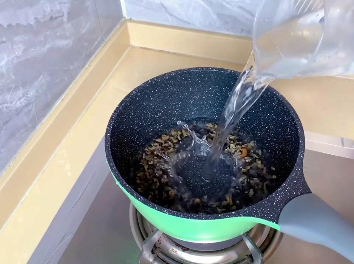 Wlewanie czystej wody z plastikowej miarki do zielonego garnka na kuchence gazowej.
