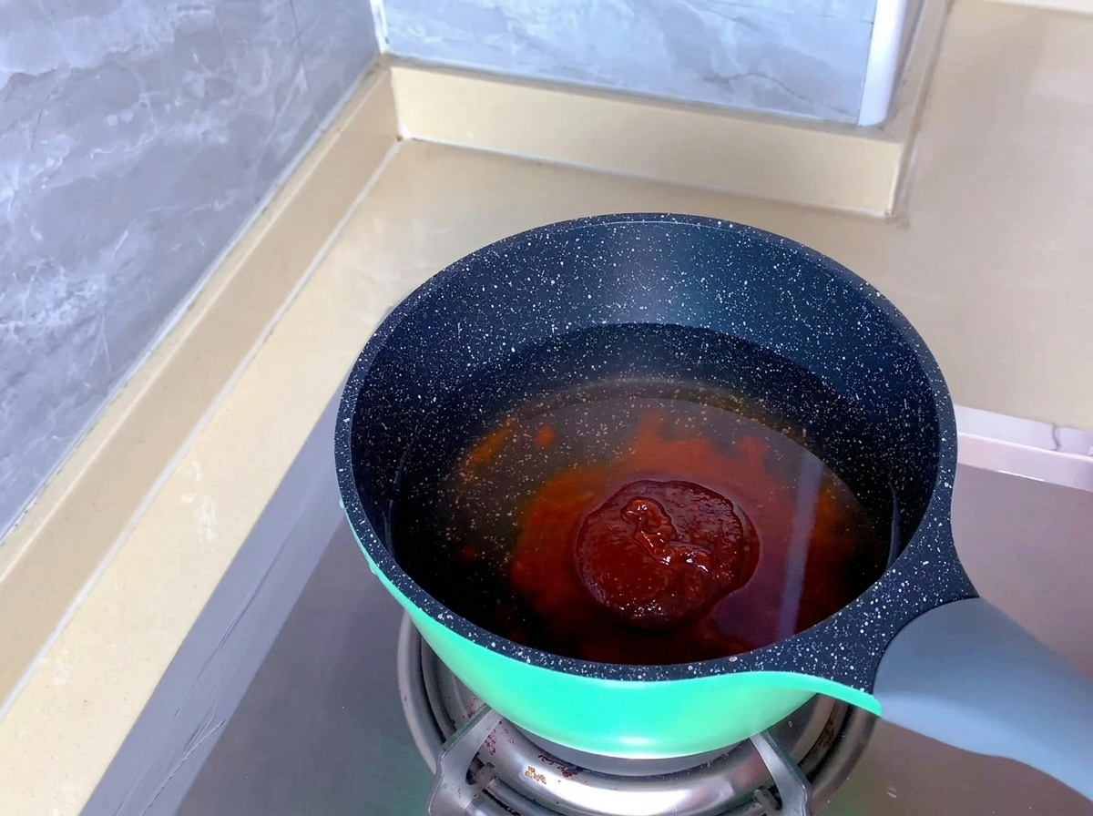 Czerwono-pomarańczowa pasta do kimchi zanurzona w czystej wodzie w nakrapianym garnku.