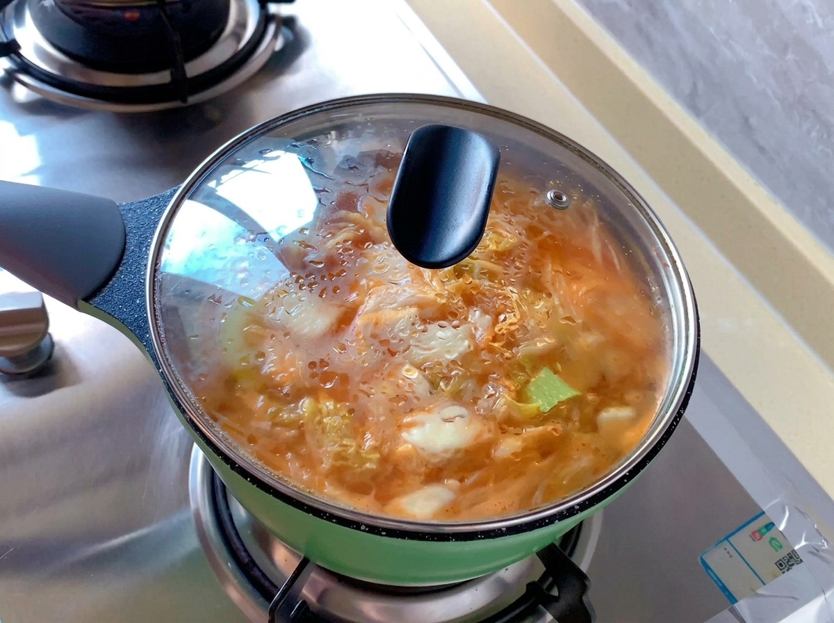 Mały zielony garnek z pomarańczową zupą kimchi pod szklaną pokrywką pokrytą skroploną parą.
