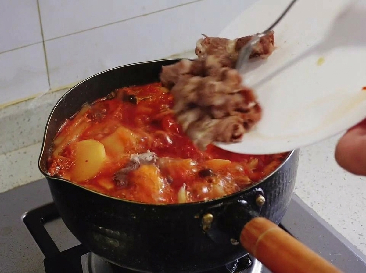 Zblanszowane kawałki tłustej wołowiny zsuwane z białego talerza do wrzącego garnka z gulaszem kimchi.