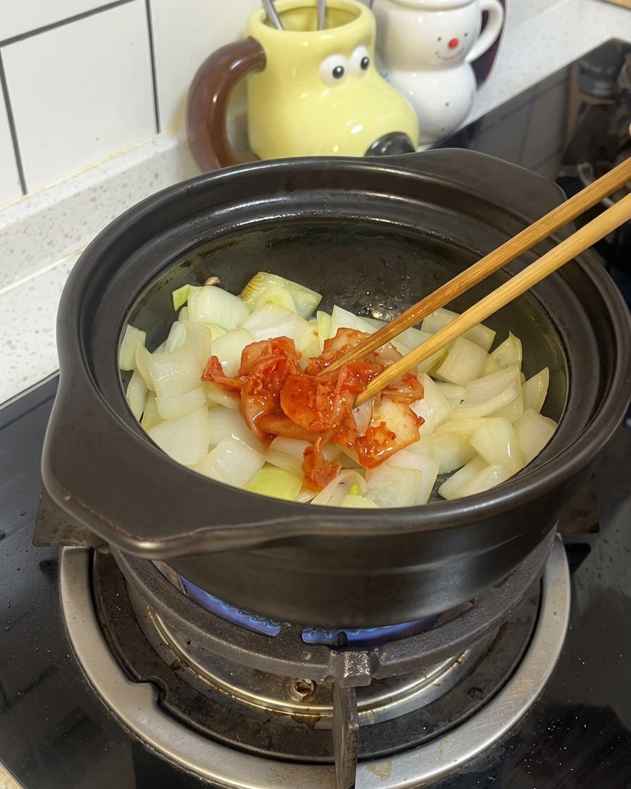 Drewniane pałeczki kładące porcję czerwonego, sfermentowanego kimchi na zeszklonej cebuli.