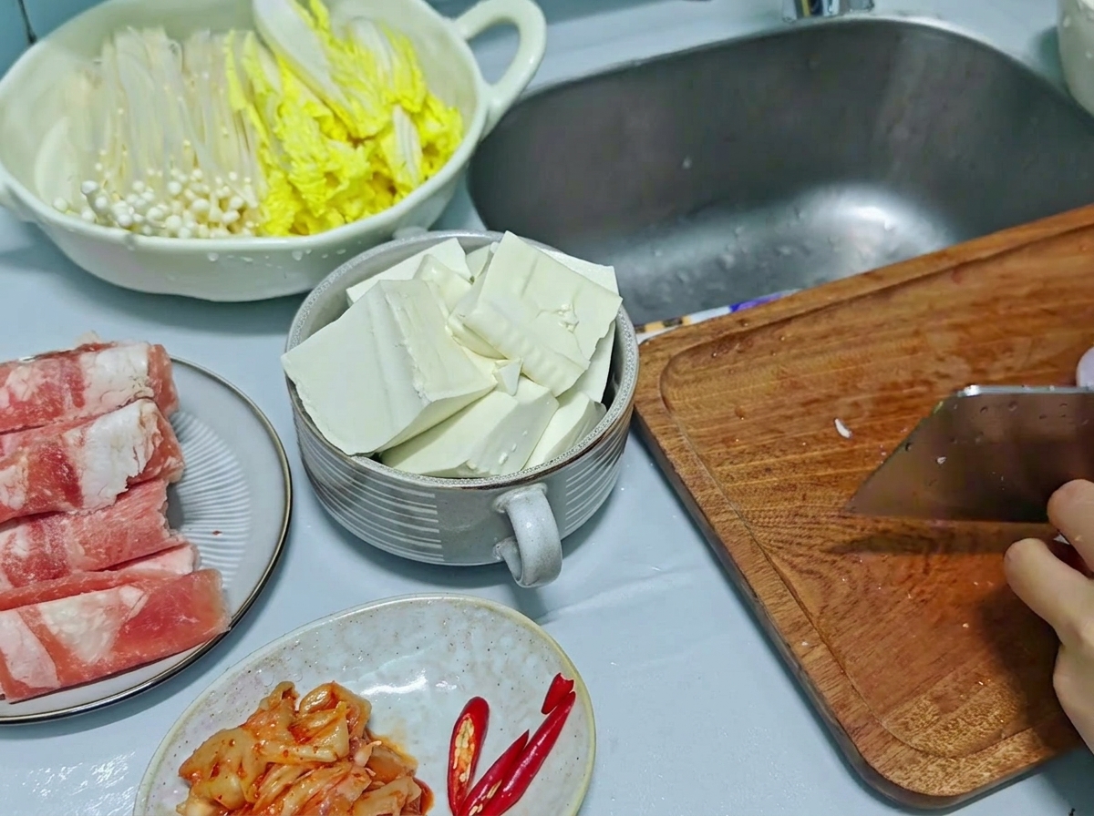 Nóż szefa kuchni siekający czerwoną cebulę i papryczkę chili na drewnianej desce, z pokrojonym tofu widocznym w misce obok.