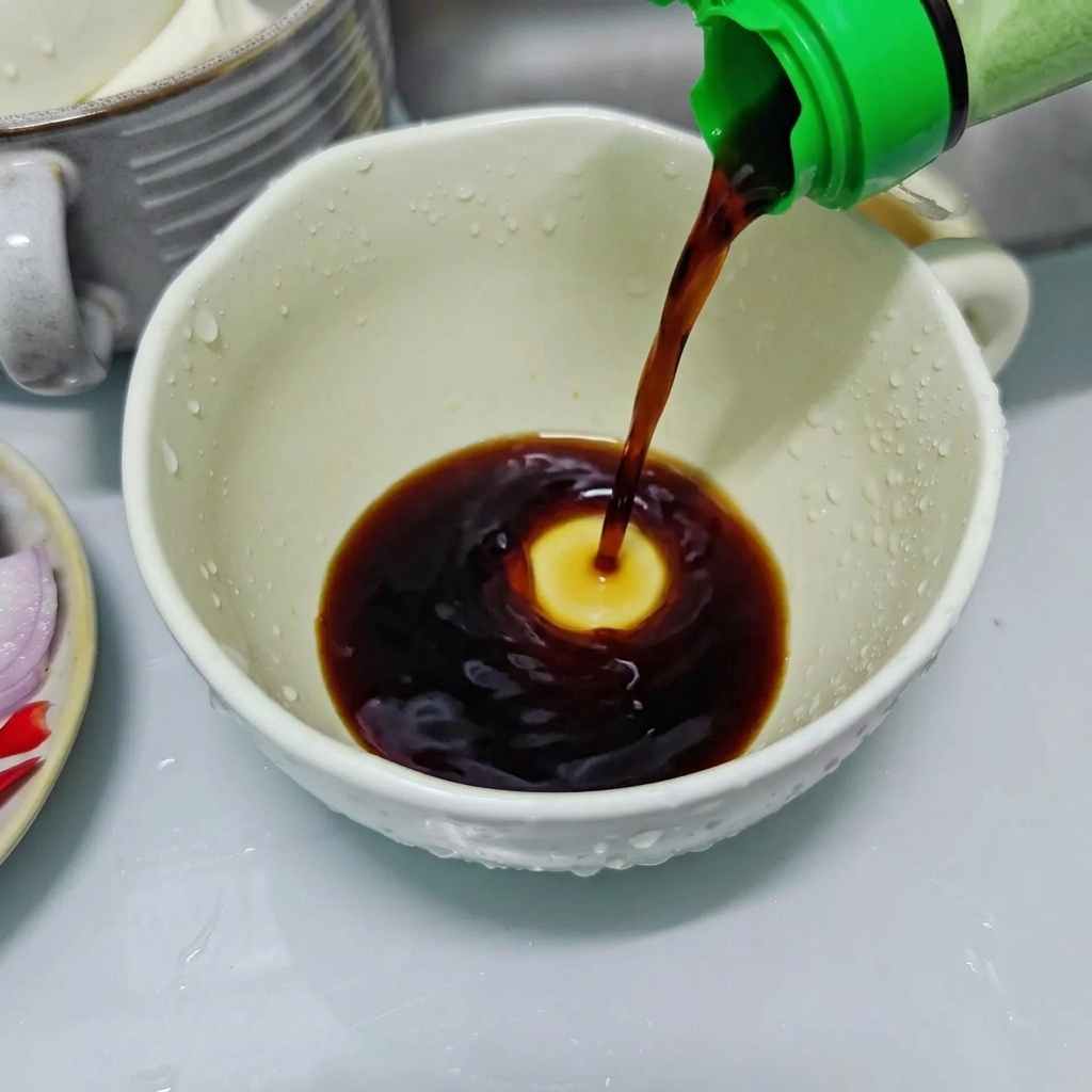 Jasny sos sojowy nalewany z butelki z zieloną zakrętką do białego ceramicznego kubka w celu przygotowania sosu doprawiającego.