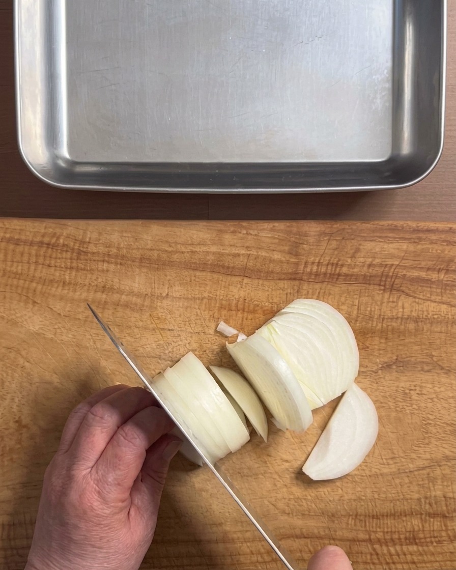 Dłonie krojące białą cebulę nożem na grube piórka na drewnianej desce kuchennej.