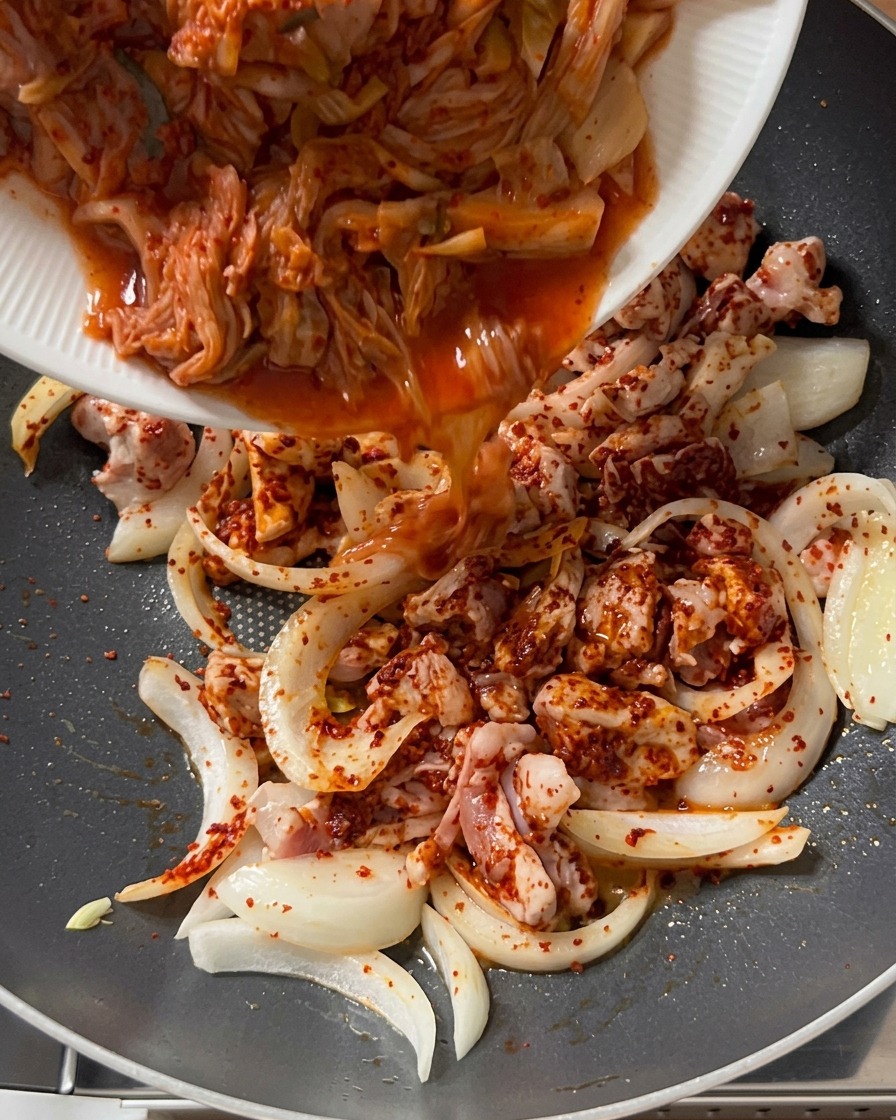 Pokrojone kimchi przekładane z białego talerza na patelnię z doprawioną wieprzowiną i cebulą.