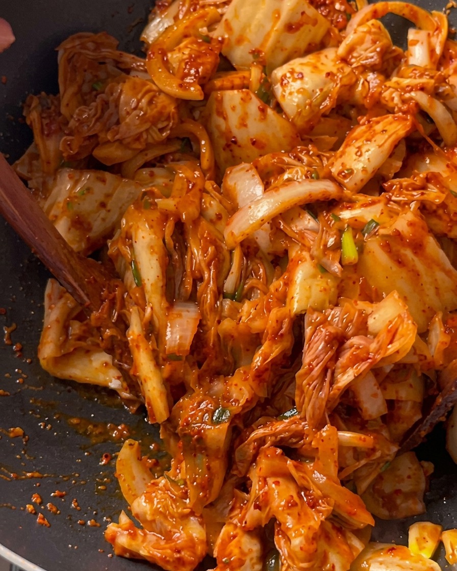 Kawałki kimchi smażone razem z wieprzowiną i cebulą w głębokim czarnym woku przy użyciu drewnianej łopatki.