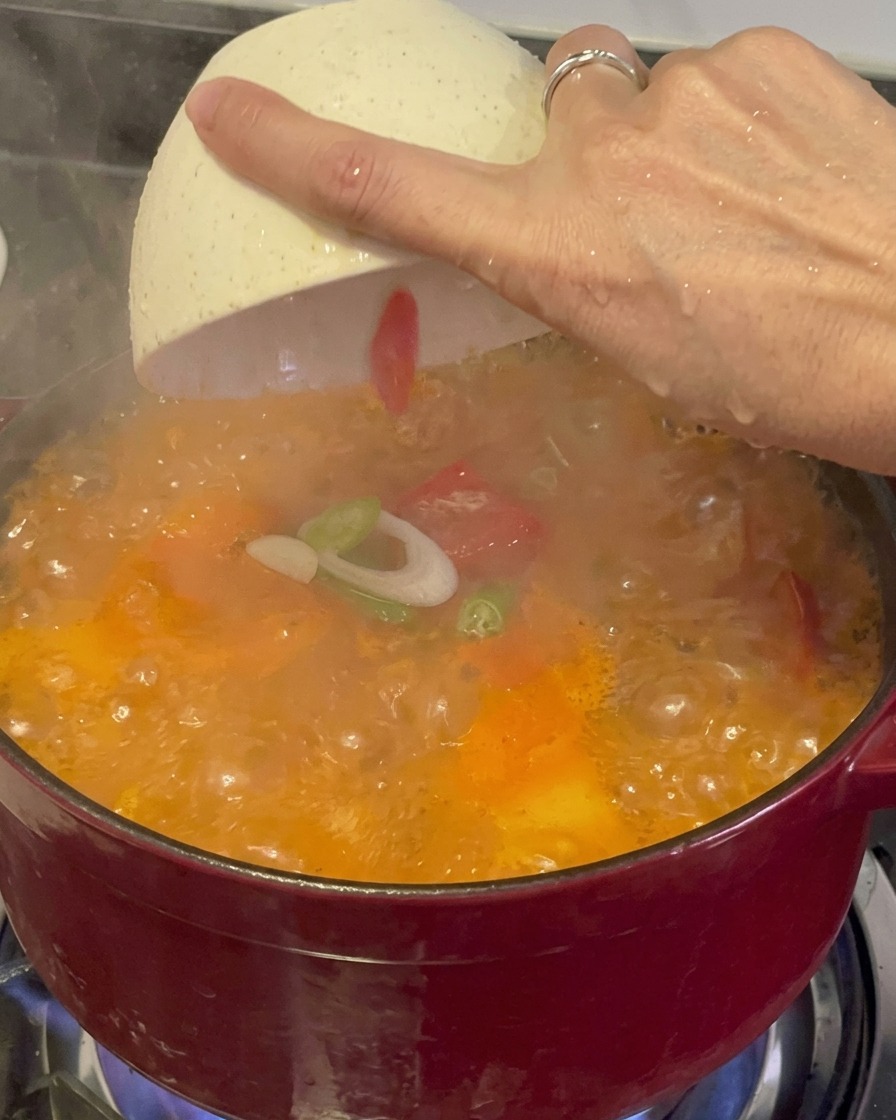 Świeżo pokrojona zielona dymka i czerwone chili posypywane z białej miseczki na parujący, bulgoczący czerwony gulasz kimchi.