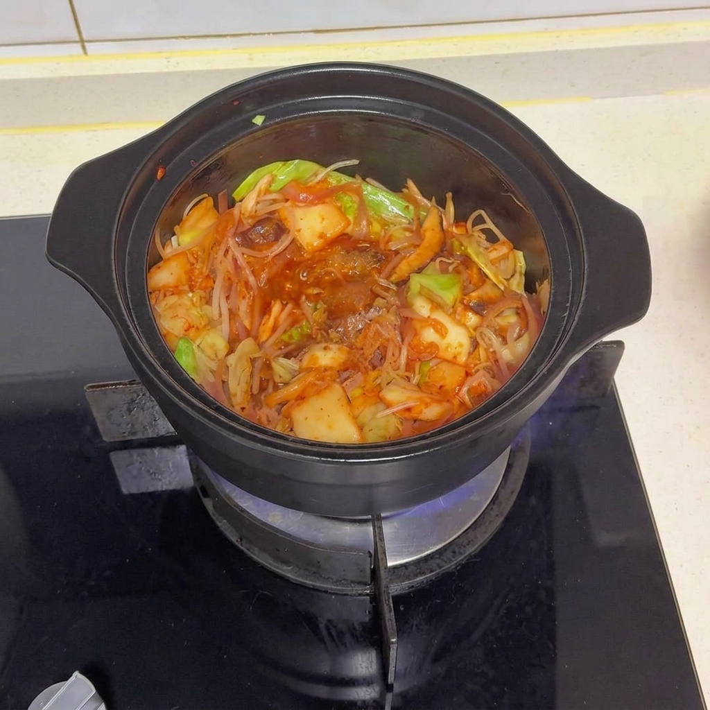 Czarny garnek pełen podsmażonych warzyw i kimchi, posypany różnymi przyprawami i czerwonym chili w proszku.