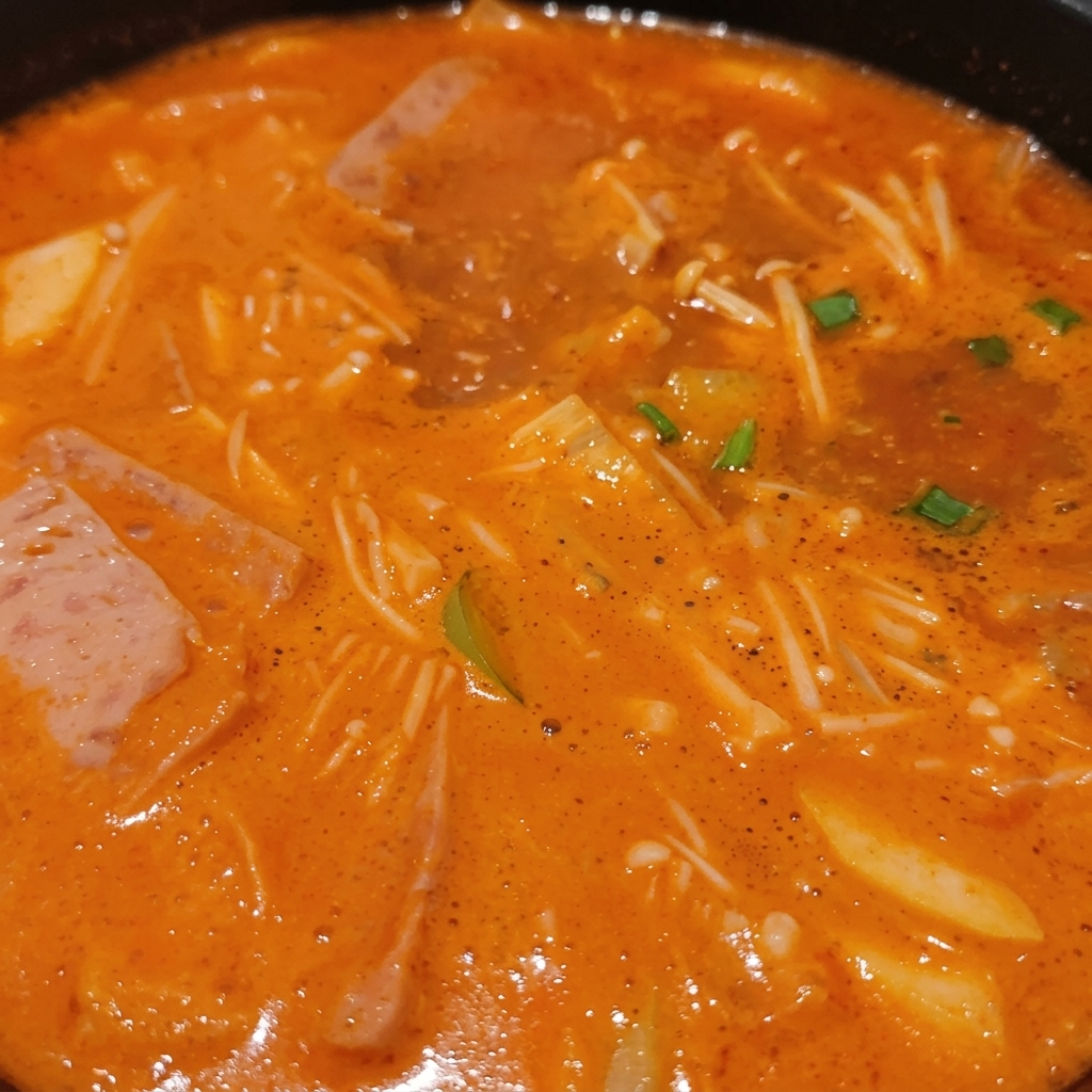 Bulgoczący koreański gulasz pełen grzybów enoki, plastrów mięsa, zielonej dymki i tofu zanurzonych w bogatym, pomarańczowym bulionie.