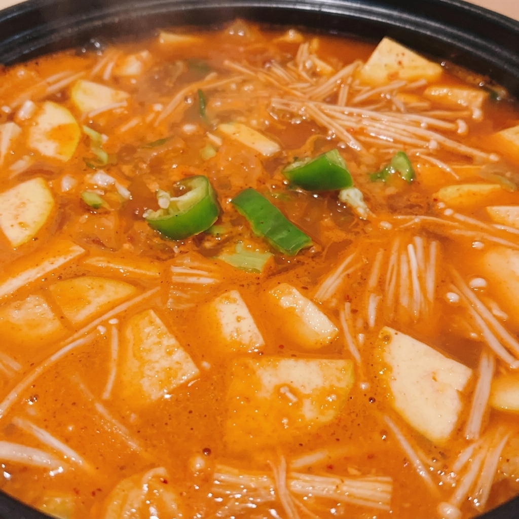 Czarny garnek z mrugającym koreańskim gulaszem z pasty sojowej, posypanym krążkami świeżego zielonego chili.