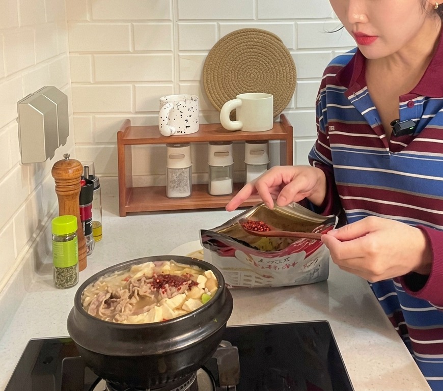 Łyżka grubo mielonego czerwonego chili dodawana do bulgoczącego glinianego garnka z koreańskim gulaszem z pasty sojowej, tofu i wołowiny.